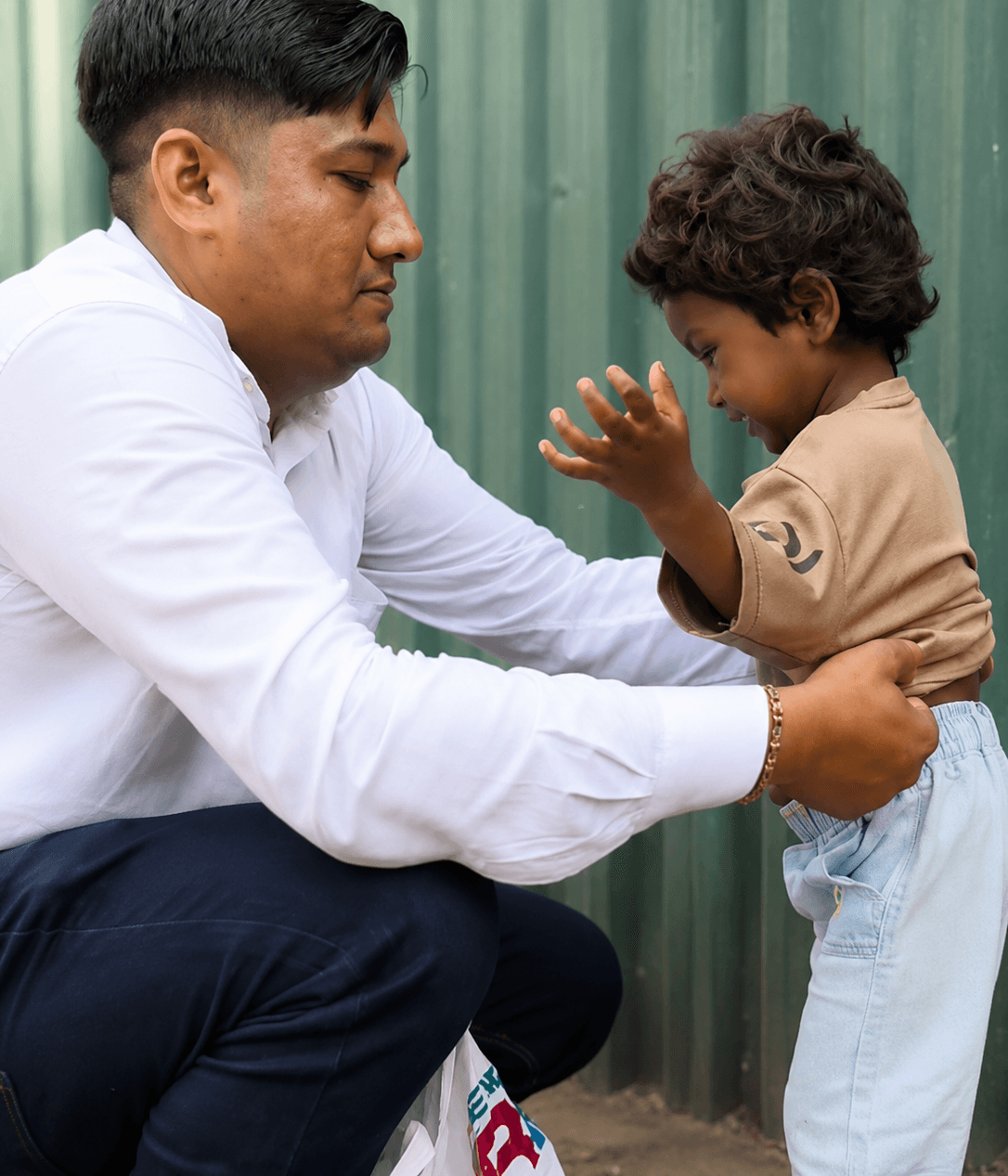 A volunteer crouches to steady a small child by the waist as the child reaches up towards him.