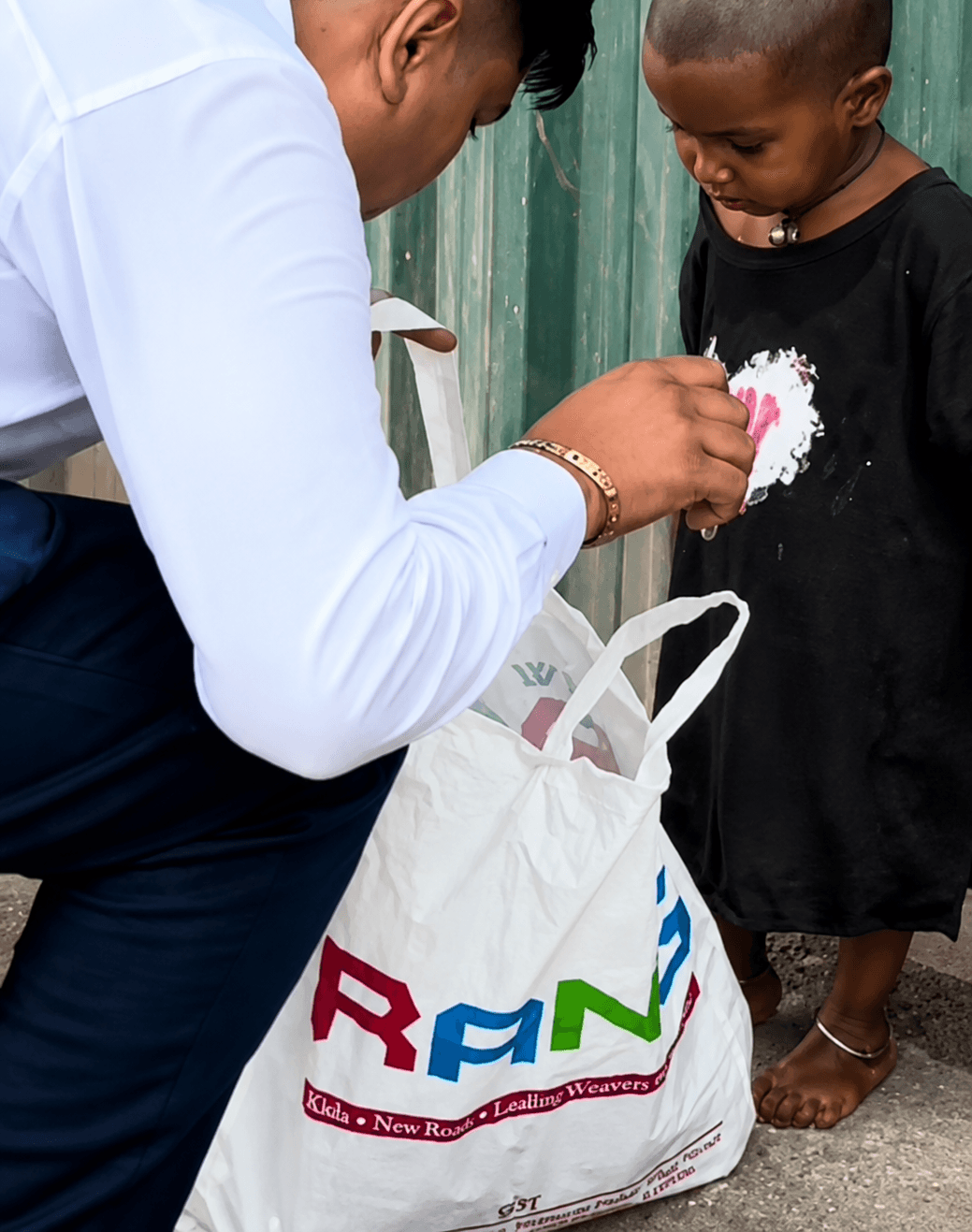 A volunteer wipes a child's hands clean while holding a bag of supplies at his side.